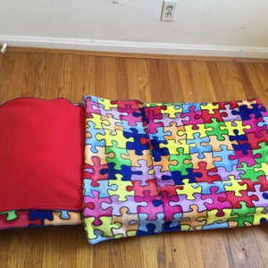 May include: A colorful puzzle-piece patterned bed set with a red pillow. The set includes a blanket and a pillow, both featuring a vibrant jigsaw puzzle design in various colors. The bed set is designed for comfort and visual appeal.