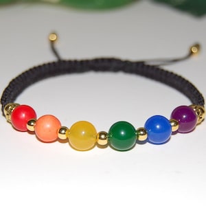 May include: A rainbow-coloured beaded bracelet with a black woven band. The bracelet features seven round beads in red, orange, yellow, green, blue, and purple, separated by gold-coloured beads. The bracelet is adjustable.