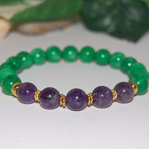May include: A beaded stretch bracelet featuring a series of smooth, round green beads interspersed with five deep purple amethyst beads. The purple beads are separated and accented by small, textured gold-toned metal spacer rings.
