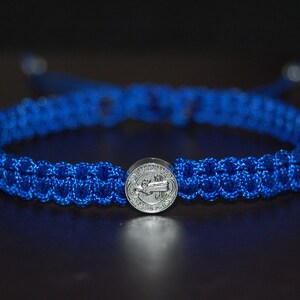 Puede incluir: Una pulsera trenzada azul con un dije de medalla de San Benito de plata.