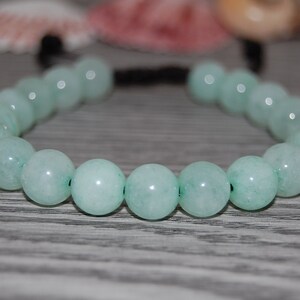 Puede incluir: Un brazalete de cuentas de color verde claro con cierre de cordón negro. Las cuentas son redondas y lisas.
