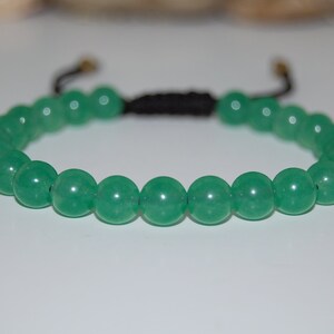 Puede incluir: Un brazalete de cuentas de jade verde con un cordón negro y detalles en metal dorado.