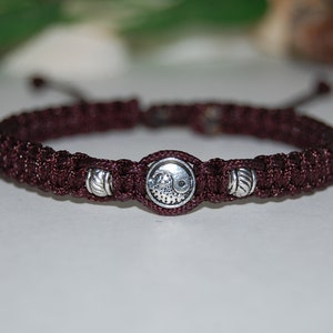 Può includere: Un braccialetto intrecciato marrone scuro con perline d'argento e un ciondolo d'argento con un simbolo yin yang.