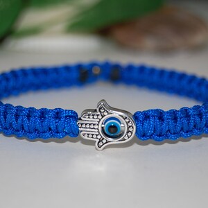 Puede incluir: Una pulsera de paracord azul con un dije de mano de Hamsa plateado con un ojo turco azul.