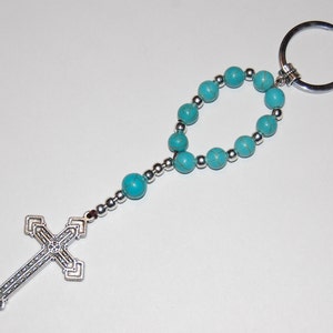 May include: A turquoise blue beaded keychain with a silver cross charm and a silver key ring.