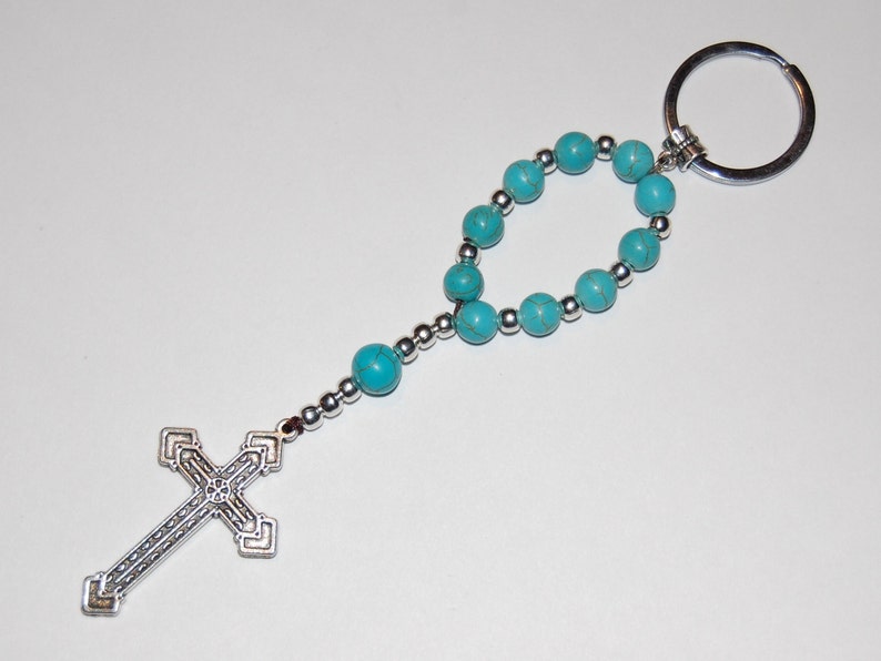 May include: A turquoise blue beaded keychain with a silver cross charm and a silver key ring.