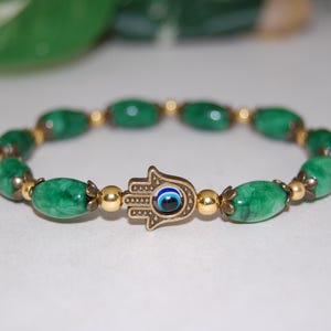 Pode incluir: Pulseira de contas de pedra verde com um amuleto de mão de hamsa dourado com um olho turco azul no centro.