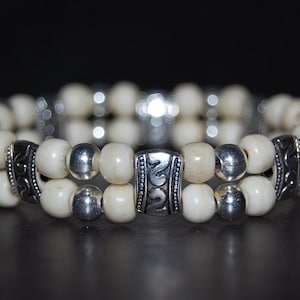 May include: A double-strand bracelet with white beads and silver accents. The silver beads have a decorative design.