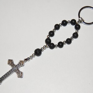 May include: A black lava rock beaded keychain with a silver cross charm and a silver key ring.