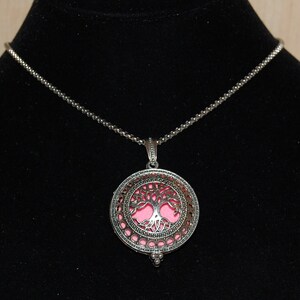 May include: A silver chain necklace with a round pendant featuring a cutout tree design. The pendant has a pink background.