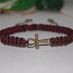 May include: A dark brown braided bracelet with a gold-toned Ankh charm.