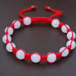 May include: A red string bracelet with white beads. The bracelet is tied with a knot and has a tassel on the end.