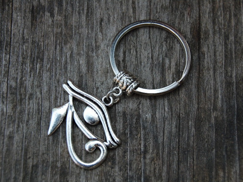 May include: Silver key chain with a silver eye of Horus charm. The charm is detailed with intricate lines and a raised eye.
