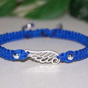 May include: A blue macrame bracelet with a silver wing charm. The bracelet features a woven design and small silver beads at each end. The wing charm is a detailed, openwork design. A stylish accessory.