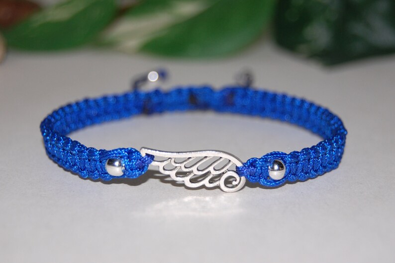 May include: A blue macrame bracelet with a silver wing charm. The bracelet features a woven design and small silver beads at each end. The wing charm is a detailed, openwork design. A stylish accessory.