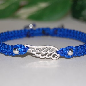 May include: A blue macrame bracelet with a silver wing charm. The bracelet features a woven design and small silver beads at each end of the charm. The wing charm is a detailed, openwork design.