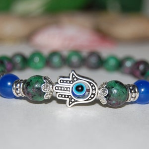 May include: A green and blue gemstone bracelet with a silver hamsa hand charm featuring a blue evil eye.