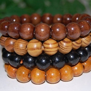 May include: Four stacked wooden bracelets with different patterns and colors. The top bracelet is brown, the second is brown and white striped, the third is black, and the bottom is light brown.