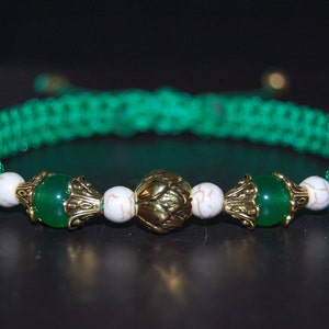 Puede incluir: Un brazalete trenzado verde con cuentas blancas y verdes y detalles dorados.