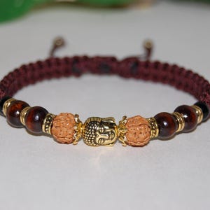 May include: A brown braided bracelet with gold beads and a gold Buddha head charm.