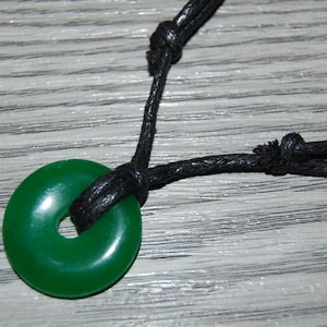 May include: A green jade pendant in the shape of a circle, with a hole in the centre, hanging from a black cord.
