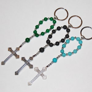 May include: Three keychains with different colored beads and silver cross charms. The beads are green, black, and turquoise.