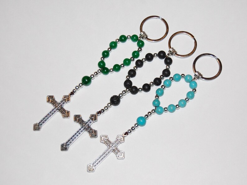 May include: Three keychains with different colored beads and silver cross charms. The beads are green, black, and turquoise.
