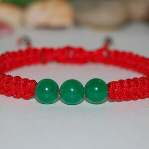 Puede incluir: Pulsera trenzada roja con tres cuentas de jade verde.
