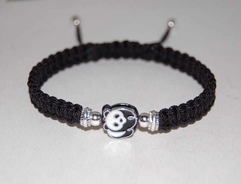 Puede incluir: Pulsera trenzada negra con un dije de plata con dise&ntilde;o de oso panda.