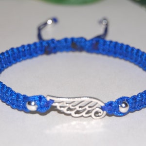 May include: A blue macrame bracelet with a silver wing charm. The bracelet is adjustable with sliding knots and features silver beads at each end. The wing charm is centered on the bracelet.