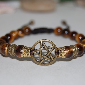 May include: A brown and gold beaded bracelet with a pentagram charm. The bracelet is made with tiger's eye beads and has a dark brown cord.