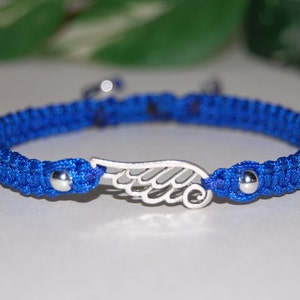 May include: A blue macrame bracelet with a silver wing charm. The bracelet features a woven design with a silver bead on each end of the wing charm. The bracelet is approximately 7 inches in length.