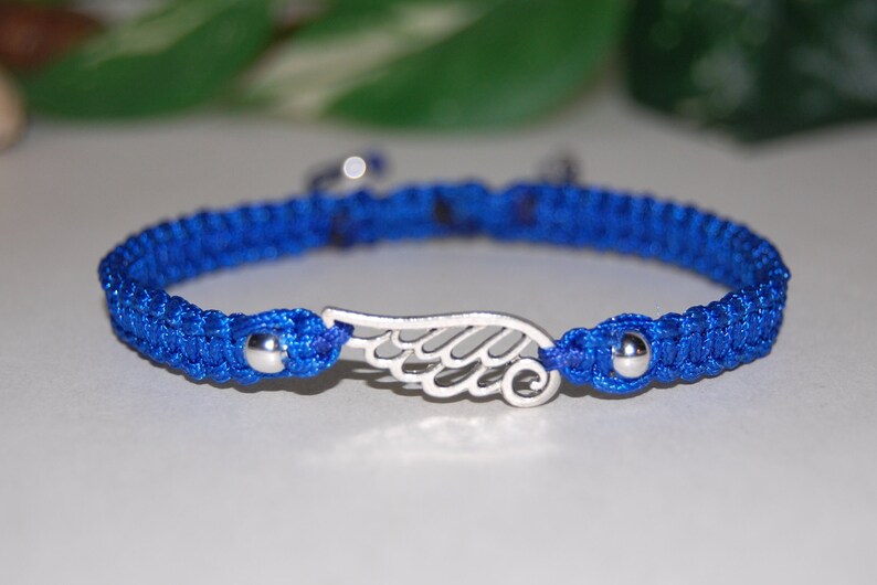 May include: A blue macrame bracelet with a silver wing charm. The bracelet features a woven design with a silver bead on each end of the wing charm. The bracelet is approximately 7 inches in length.