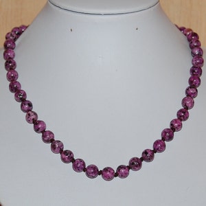 May include: A purple and white speckled bead necklace. The necklace is made of round beads and is strung on a thin cord.