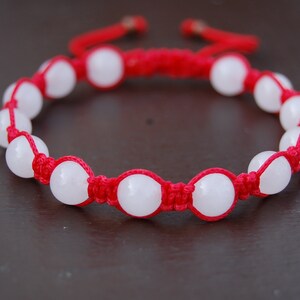 May include: A red string bracelet with white round beads. The bracelet is tied with a knot.