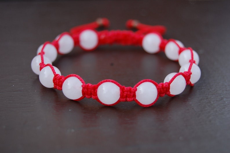 May include: A red string bracelet with white round beads. The bracelet is tied with a knot at the end.