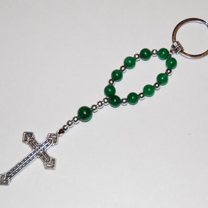 May include: A silver key chain with a green beaded rosary and a silver cross charm.