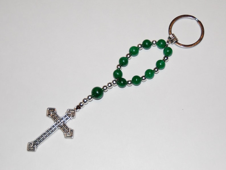 May include: A silver key chain with a green beaded rosary and a silver cross charm.