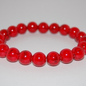 May include: A red beaded bracelet with a glossy finish. The beads are round and have a slight marbling effect.