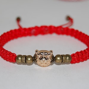 Puede incluir: Pulsera de cuerda roja con un dije de tigre dorado y dos cuentas doradas.