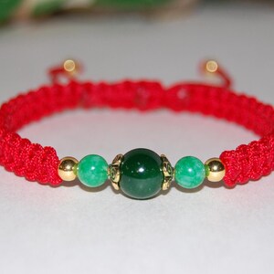 Puede incluir: Pulsera de cuerda roja con una cuenta de jade verde y detalles dorados.