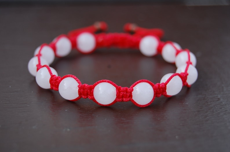 May include: A red string bracelet with white round beads. The bracelet is knotted with a simple design.