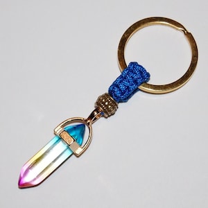 May include: A rainbow crystal point keychain with a gold-tone metal setting and a blue braided cord attached to a gold-tone key ring.