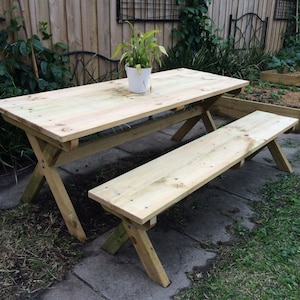 May include: A wooden picnic table with a bench. The table is made of natural wood and has a simple, rustic design. The bench is also made of wood and is attached to the table.