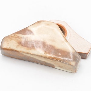 May include: A ceramic ring holder in the shape of a triangle with a brown and white marbled glaze. The ring holder is open on one side and has a small hole in the top for a ring.