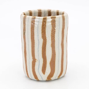 May include: A white ceramic cup with brown stripes. The cup has a textured surface.
