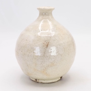May include: A small, off-white ceramic vase with a rounded body and a narrow neck. The vase has a speckled texture and a slightly uneven surface, giving it a rustic appearance. The base is a darker shade of the same color.