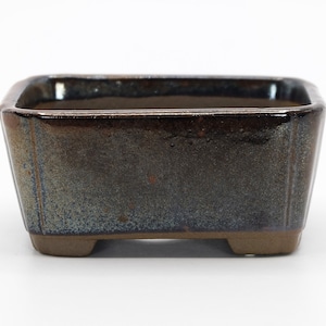 Può includere: Un vaso rettangolare per bonsai in ceramica con una smaltatura marrone scuro e un riflesso iridescente blu chiaro. Il vaso ha quattro piccoli piedini.