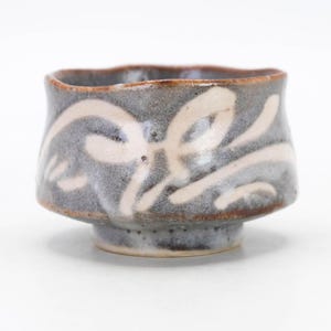 May include: A small, gray ceramic bowl with a white glaze and a wavy design. The bowl has a slightly flared rim and a rounded base.
