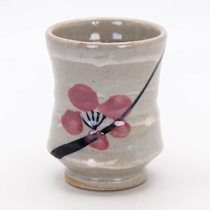 May include: A handmade ceramic cup with a light gray glaze. The cup features a red floral design with black accents. The cup has a unique shape and is suitable for beverages.